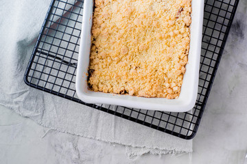 Apple crumble in white ceramic form on gray table background. Fruit pie on grate for cooling. Top...