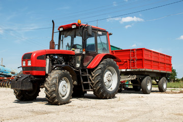 Obraz premium Red tractor with trailer parked on a farmyard