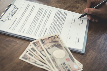 Hand holding pen about to sign contract with money, Japanese yen banknotes, on the table