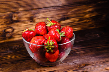 Ripe strawberries in glass bowl on wooden table