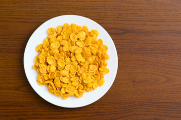 Corn flakes. 
Closeup of a plate of golden cornflakes on wooden table.