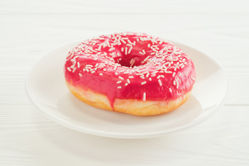 One pink donut, close-up. Donut on a plate on white wooden table. Delicious breakfast, sweet donut with copy space. 