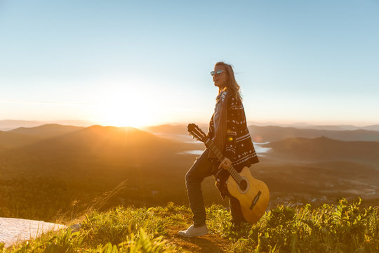 Young girl meets sunrise on top of a mountain with a guitar 