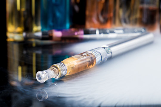 Electronic cigarette with e-liquid bottles in background