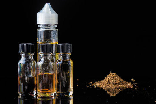 E-liquid bottles next to grinded tobacco leaves and smoke cloud