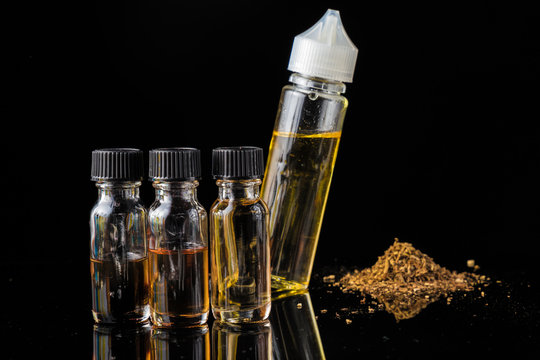 E-liquid bottles next to grinded tobacco leaves and smoke cloud