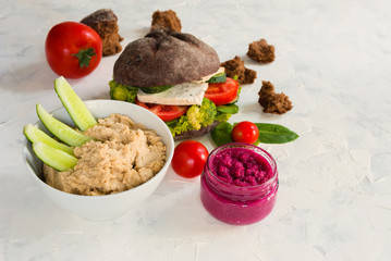 Vegan tofu berger on white background. Lettuce, tomatoes, cucumber, salad, whole wheat bread, hummus.