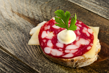 Sandwich with salami and a sprig of parsley on a wooden background.