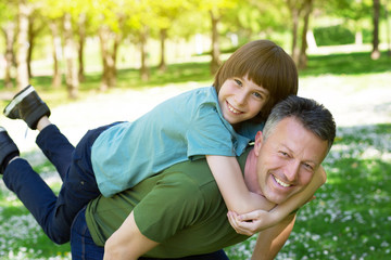 Portrait of father with his son having fun in summer park. Piggyback. Family fun. Happy boy playing with dad summer nature outdoor