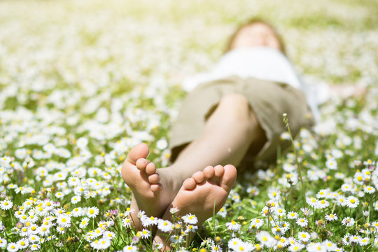 Child's feet in daisy closeup view. Shoeless boy. Little boy lying on summer meadow green grass with daisy.