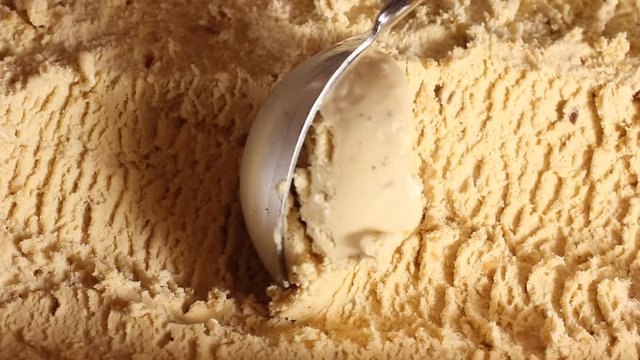 Taking a scoop of ice cream from the box. Close-up of caramel ice cream in a large box. Round spoon makes shoelaces balls for buyers