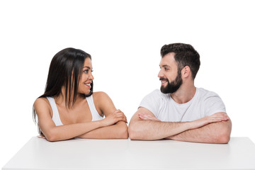 Happy young multiethnic couple sitting at white table and smiling each other