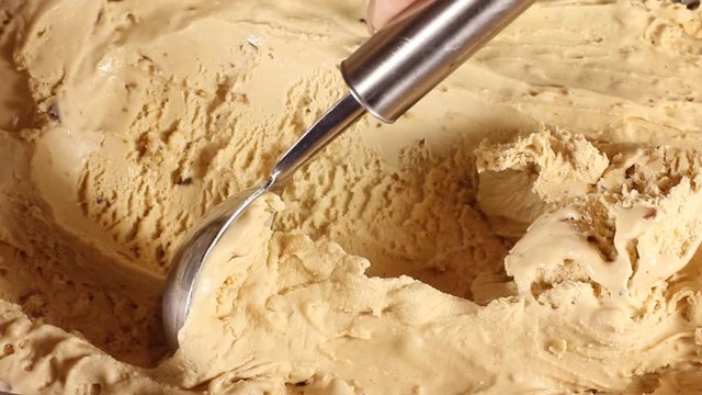 Taking a scoop of ice cream from the box. Close-up of caramel ice cream in a large box. Round spoon makes shoelaces balls for buyers