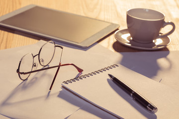 Close-up view of digital tablet with eyeglasses, cup of coffee and papers on table
