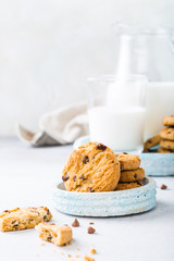 Stack of chocolate chip cookies on blue stone plate with glass of milk on light gray background. Selective focus. Copy space.
