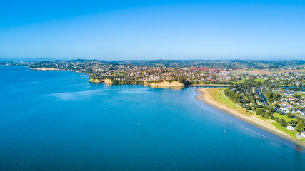 Aerial view on sunny beach with residential suburb on the background. Auckland, New Zealand.