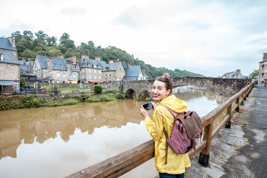 Young woman in yellow raincoat traveling with backpack and photo camera in Dinan village at Brittany region in France