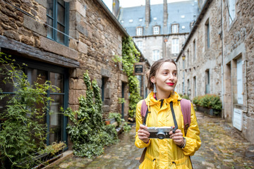 Young woman in yellow raincoat walking with backpack and photo camera in Dinan village at Brittany...