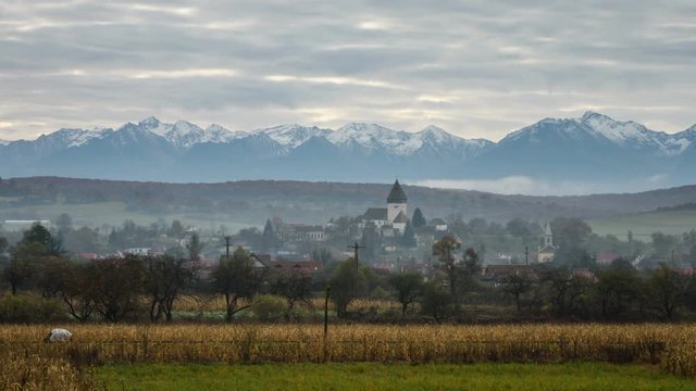 Early autumn countryside view with Hosman medieval village and Fagaras Mountains in backgorund. 4K Timelapse.