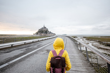Young female traveler in yellow raincoat on the road to famous saint Michel island in France