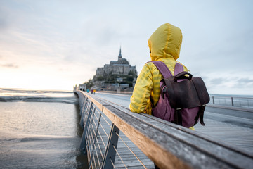 Young female traveler in yellow raincoat on the road to famous saint Michel island in France