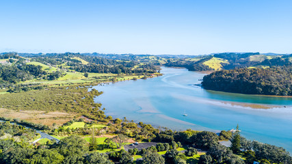 Aerial view on a river running through farm land with forest and grassy meadows. Auckland, New Zealand