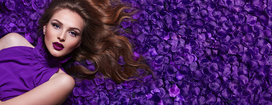 Fototapeta The girl in the petals. Beautiful young girl lies in the violet petals in a long dress. Glamor, luxe. Hair - curls. Makeup - arrows, purple lipstick. Love, romance.