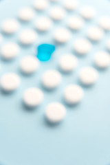 One blue liquid capsule in a grid of white tablets