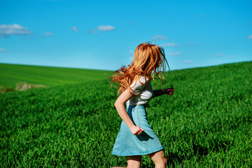 Naklejka na ściany i meble Young beautiful woman running on a green field