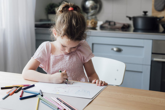 Cute little Caucasian girl drawing with crayons on kitchen table.