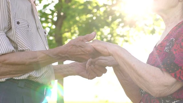 Close-up of the hands of the old grandparents in the sunny Park. Close-up grandma and grandpa holding hands in the Park at sunset.