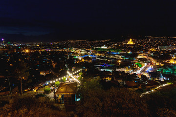 Sunset panorama view of Tbilisi, capital of Georgia country, from Narikala fortress. Famous landmarks with illumination. Tourists have dinner in restaurant with old fashioned light bulbs.