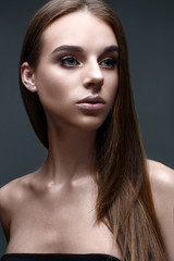 A young girl with straight flowing hair. A beautiful model with a gentle nude make-up and shining skin. Photo is taken in the studio. Gray background. Beauty of the face.