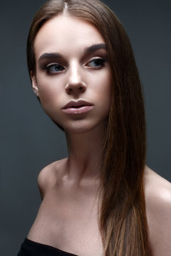 A young girl with straight flowing hair. A beautiful model with a gentle nude make-up and shining skin. Photo is taken in the studio. Gray background. Beauty of the face.