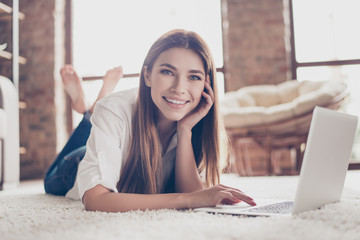 So comfortable and easy! Close up of young happy girl typing in her laptop lying on the floor on a...