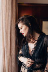 Fototapeta premium Young beautiful sexy woman in a black lace dressing gown posing in a room