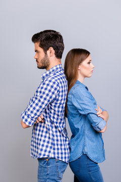 Mistrust and cheat problems. Annoyed couple is ignoring each other, standing back to back, wearing casual clothes, with crossed hands on the pure background