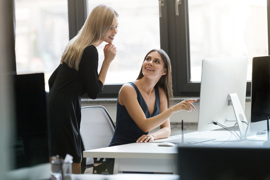 Two smiling businesswomen working with computer together