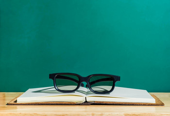 Black eyeglasses on open book on wooden table at green blackboard,leave space on top to adding your text,education concept