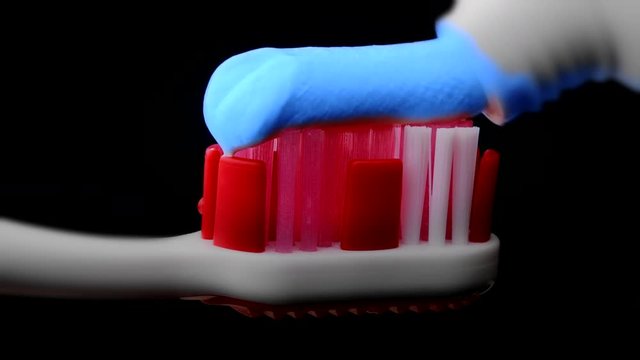 Tooth paste and brush. Applying blue toothpaste on red toothbrush against black background in slow-motion.