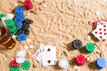 Gambling on vacation concept - white sand with seashells , colored poker chips and cards. Top view