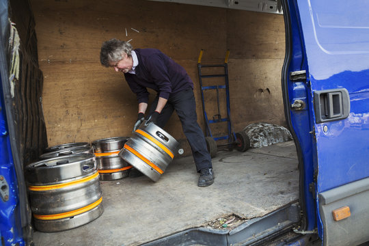 Man working in a brewery, loading metal beer kegs into a van.