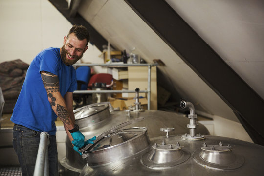 Smiling man working in a brewery, closing lid of a stainless steel tank.