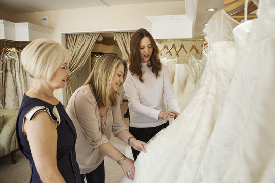 Three women, a client and two retail advisors in a wedding dress shop, looking through the choice of gowns. 