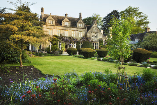 Exterior view of a 17th century country house from a garden with flower beds, shrubs and trees.
