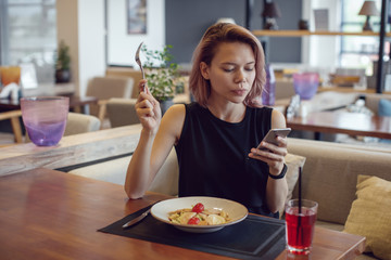 Attractive woman using smartphone and eating in a cafe.