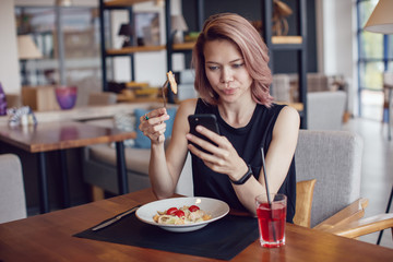 Attractive woman using smartphone and eating in a cafe.