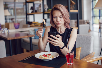 Attractive woman using smartphone and eating in a cafe.