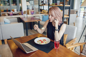 Business woman eats at a cafe and uses a smartphone and laptop.