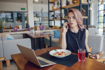 Business woman eats at a cafe and uses a smartphone and laptop.